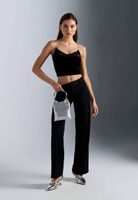 Czarny welurowy crop top na cienkich ramiączkach, czarne spodnie z wysokim stanem, metaliczna srebrna torebka z okrągłym uchwytem, srebrne szpilki w paski.