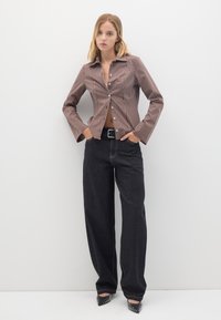 Gestreifte braune Hemdbluse mit langen Ärmeln, kombiniert mit weit geschnittenen dunkelblauen Jeans und spitzen schwarzen Pumps mit Nieten.