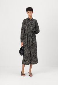 Black paisley-patterned midi dress with a belt at the waist, long sleeves, and a collared neckline. Paired with a black handbag and sandals.