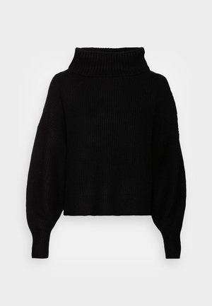 Pull en maille côtelée noire avec manches longues surdimensionnées et large col montant sur un fond gris clair.