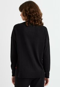 Maglione nero lavorato a maglia con maniche lunghe, vestibilità rilassata, orlo a costine e un sottile dettaglio rosso vicino al fondo. Texture liscia.