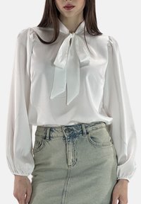 Witte satijnen blouse met lange ballonmouwen en een striksluiting bij de hals. Gecombineerd met een lichtblauwe denim rok met een voorsplit.