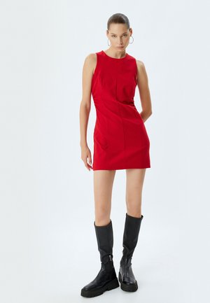 Abito senza maniche rosso con una silhouette aderente e dettagli delle cuciture, abbinato a stivali in pelle nera al ginocchio con dettagli in zip.