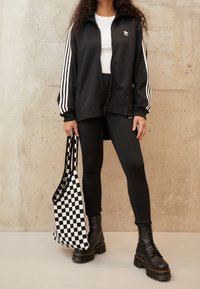 Svart zip-up jacka med vita ränder, svarta leggings, svarta snörstövlar och en svartvit rutig tote-väska.