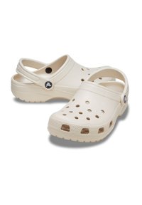 Light beige clogs made of plastic with a ventilated design, featuring multiple holes, a back strap, and a textured footbed for comfort.