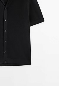 Cardigan noir à manches courtes tricoté avec fermeture boutonnée devant et motif texturé du tissu.