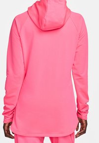 Sudadera rosa con mangas largas, hecha de una tela suave. Cuenta con una capucha central y un dobladillo trasero más largo. Sin patrones ni acentos visibles.