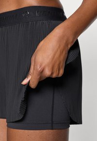 Μαύρο αθλητικό σορτς με πλισέ σχέδιο και ελαστική μέση. Το ύφασμα φαίνεται ελαφρύ και ελαστικό, με λείο εσωτερικό επένδυση.