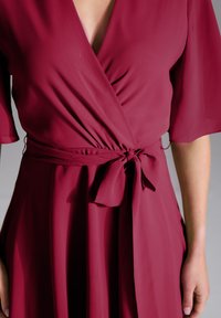 Robe enveloppante bordeaux en tissu léger, dotée de manches courtes, d'une ceinture nouée à la taille et de drapés doux.