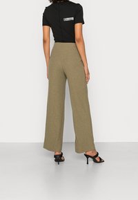 Pantalons larges en khaki côtelé avec une taille haute, associés à un t-shirt noir ajusté avec un petit motif dans le dos.