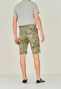 Pantalones cortos de camuflaje en verde oliva, con múltiples bolsillos, un corte relajado y un dobladillo por encima de la rodilla. Combinados con una camiseta gris.