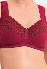 Soutien-gorge bordeaux avec larges bretelles, panneau en dentelle florale en haut, un petit nœud en satin au centre et une finition lisse.