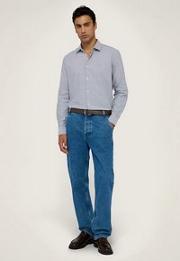 Camicia azzurra chiusa con bottoni, jeans di denim blu, cintura nera e scarpe nere. Vestibilità casual, maniche lunghe e tessuto dalla trama liscia.