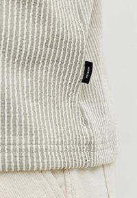 Tissu texturé beige et blanc avec des rayures verticales et une petite étiquette noire marquée « PREMIUM » près de l'ourlet.