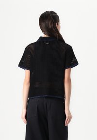 Black short-sleeve shirt made of open mesh fabric. Features a blue accent along the collar and hem. Slightly loose fit and cropped design.