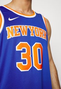 Niebieski strój koszykarski z napisem "NEW YORK" w pomarańczowych, blokowych literach oraz numerem "30" w białym, pomarańczowym obrysie. Posiada okrągły dekolt i logo Nike.