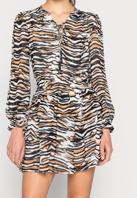 Robe à manches courtes plissée en tissu transparent avec un motif de rayures de tigre noir, blanc et orange. Encolure nouée avec des franges décoratives.