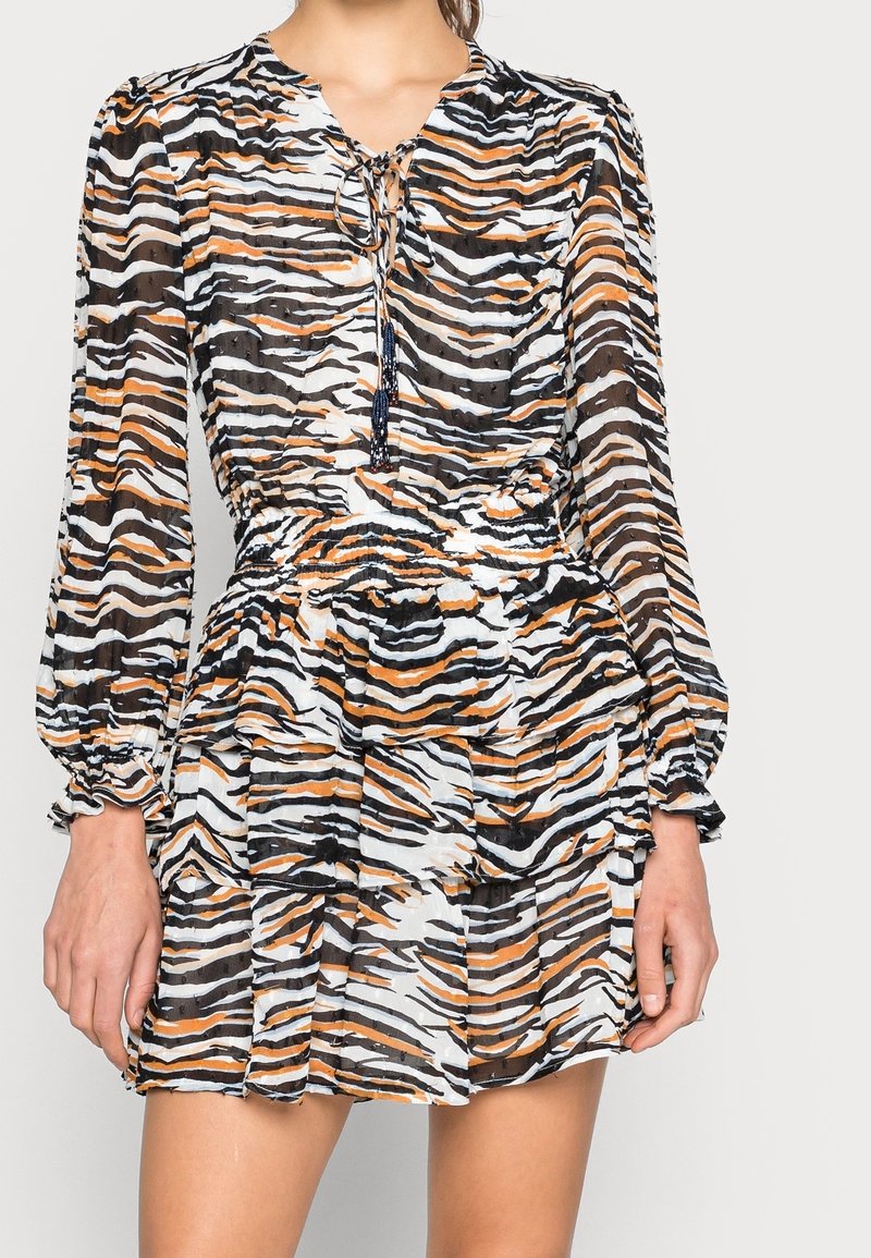 Robe à manches courtes plissée en tissu transparent avec un motif de rayures de tigre noir, blanc et orange. Encolure nouée avec des franges décoratives.