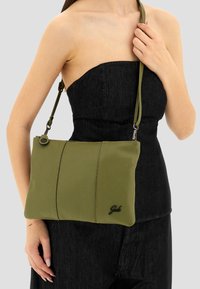 Borsa a tracolla verde in pelle con finitura testurizzata, dotata di cerniera superiore e accentuazione nera del logo. Tracolla regolabile. Design rettangolare semplice.