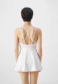 White athletic dress with a flared skirt, featuring a crisscross back strap design and smooth texture. Suitable for active wear.