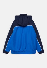 Blue and navy windbreaker jacket with elastic cuffs and hem, white piping detail, and attached hood, shown from the back.
