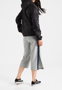 Kamo-mönstrad svart huva jacka, gråa korta sweatpants med marinblå sidostreck, och svarta sneakers med vita sulor.