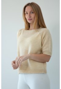 Sweter na krótki rękaw w kolorze kremowym, z ribbowanym dołem i okrągłym dekoltem, o miękkim, teksturowanym wykończeniu.