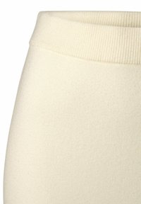 Leggings di un morbido color crema con una ampia fascia a coste, realizzati in un tessuto liscio e testurizzato con una forma aderente.