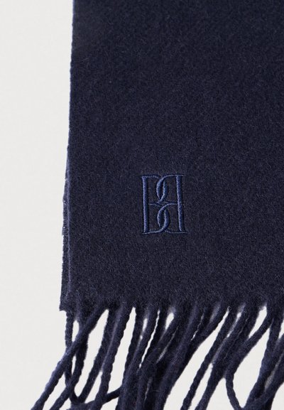 Εσάρπα από μαλλί σε ναυτικό μπλε χρώμα με φουντωτά άκρα, διακοσμημένη με λογότυπο κεντημένο στο ίδιο χρώμα. Μαλακή υφή με ομαλή επιφάνεια.