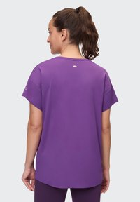 Lila kurzärmliges Sportoberteil mit rundem Halsausschnitt und lockerer Passform. Glatte Fabric, abgerundeter Saum und ein kleines Logo-Detail auf der Rückseite.