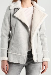 Veste en mélange de laine grise avec un col et une doublure en fausse fourrure blanche. Présente une fermeture éclair à l'avant et deux poches latérales. Fini texturé avec des accents cousus.