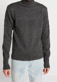 Harmaa korkeakauluksinen neule, jossa on riduttua kaula-aukossa ja teksturoitu kuvio rinnassa. Sovitettu hihnat ja helma, pehmeä neulekangas, rento muotoilu.