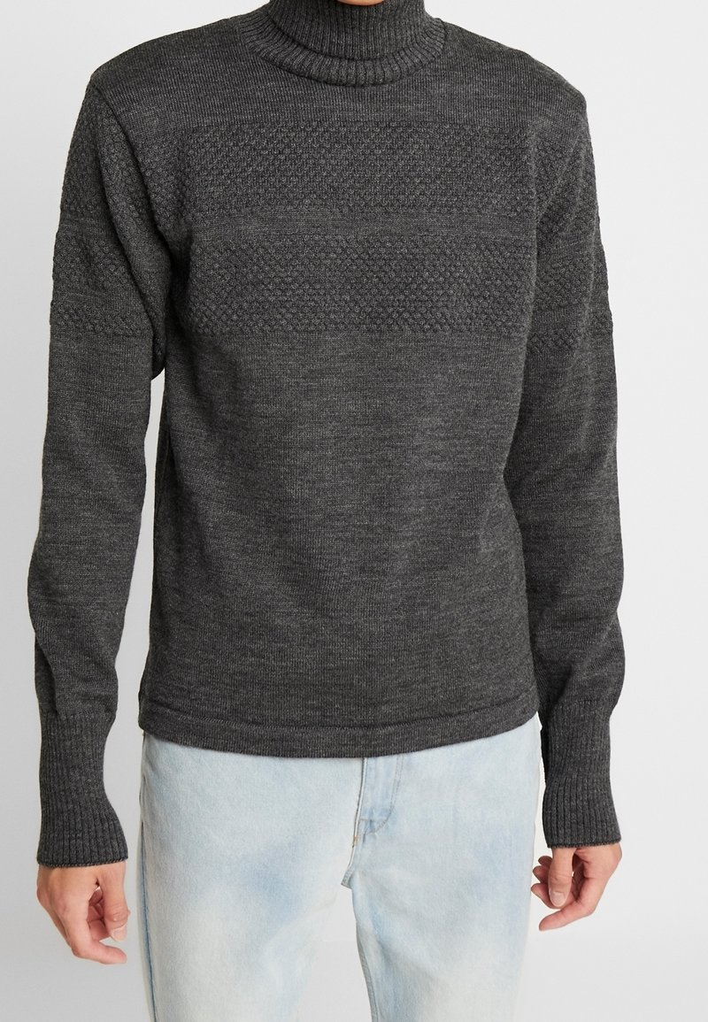 Harmaa korkeakauluksinen neule, jossa on riduttua kaula-aukossa ja teksturoitu kuvio rinnassa. Sovitettu hihnat ja helma, pehmeä neulekangas, rento muotoilu.