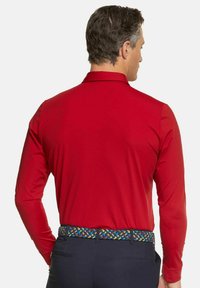 Rotes langärmliges Poloshirt aus glattem Stoff, mit Kragen und einem bunten geflochtenen Gürtel. Minimalistisches Design ohne sichtbare Logos.