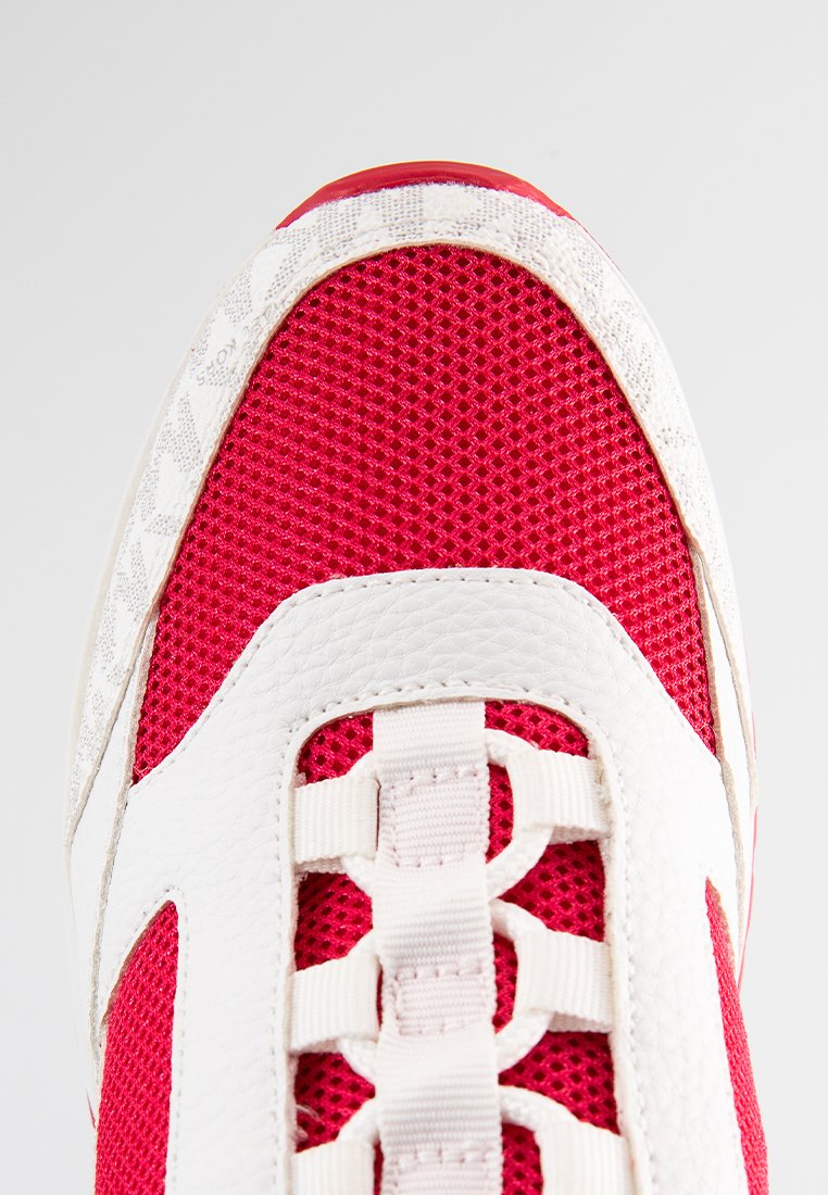 Sneaker in rete rossa con accenti in pelle bianca, caratterizzato da una parte superiore testurizzata e un sistema di allacciatura unico. La suola è minimalista e arrotondata.