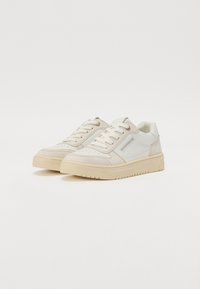 White and beige sneakers with a smooth leather and suede upper, lace-up design, perforated toe box, and thick rubber sole.