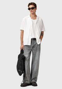 Hvid skjorte med korte ærmer, ribbet tanktop, løse grå jeans, sort bælte, sort taske, kraftige sorte sko og solbriller.