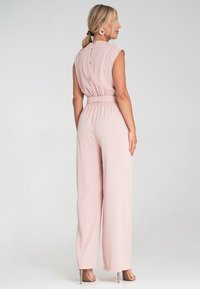 Różowy kombinezon z krótkimi rękawami, elastycznym pasem i szerokimi nogawkami. Posiada detale w postaci guzików z tyłu oraz gładką fakturę materiału.