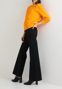 Pomarańczowa bawełniana bluza z prążkowanymi mankietami, zestawiona z czarnymi, szerokimi spodniami z wysokim stanem oraz czarnymi botkami na słupku.
