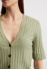 Hellgrüne, gerippte Strickjacke mit tiefem V-Ausschnitt, kurzen Ärmeln und schwarzen Knöpfen an der Vorderseite. Glatte Stofftextur.