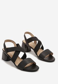 Sandales noires à talons avec un design à brides croisées, présentant un dessus texturé et une semelle intérieure en cuir lisse. Talon carré et style ouvert.
