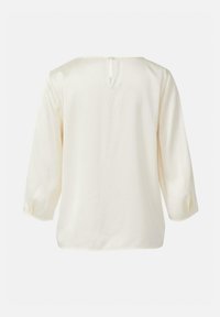 Kremowa, luźna bluzka z rękawami 3/4 i zapięciem na pętelkę z tyłu. Gładka faktura i zaokrąglony dekolt.