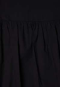 Tessuto nero con una finitura testurizzata, caratterizzato da dettagli arricciati in vita che creano una silhouette fluida. Design semplice e monocromatico.