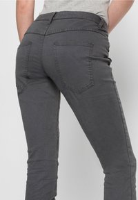 Šedé kalhoty vyrobené z měkkého materiálu, s středně vysokým pasem, tradičními zadními kapsami a úzkým, přiléhavým střihem.