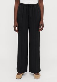 Mustat leveät housut, jotka on valmistettu kevyestä kankaasta. Niissä on joustava vyötärö, johon kuuluu nyöri ja hienovarainen pystyrakenne.