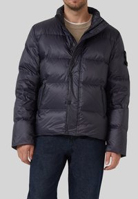 Padded jakna u tamnoplavoj boji s visokim kragnom, s kopčama na dugmadima i dva bočna zip džepa. Glatka, sjajna textura, kviltani dizajn.