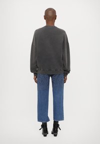 Εξαιρετικά μεγάλος γκρι φούτερ με τρύπες, συνδυασμένος με ανοιχτό μπλε τζιν που διαθέτει υφή στο κάτω μέρος. Μαύρες μπότες με τακούνι.