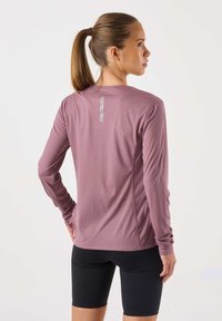 Pitkähihainen, kevyt, laventelinvärinen paita teksturoidulla kankaalla ja takana oleva logodetaili. Yhdistetty mustiin, vartalonmyötäisiin shortseihin.