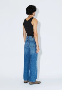 Black tank top paired with high-waisted, wide-leg blue denim jeans. Notable features include a back pocket and light fading.