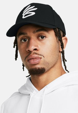 Musta lippalakki, jossa on valkoinen kirjailtu logo, jossa on tyylitellyt alkukirjaimet. Henkilöllä on päällään valkoinen huppari, jossa on nyöri.